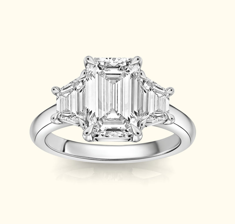 Elegant three-stone ring featuring a central emerald-cut diamond and two smaller stones.