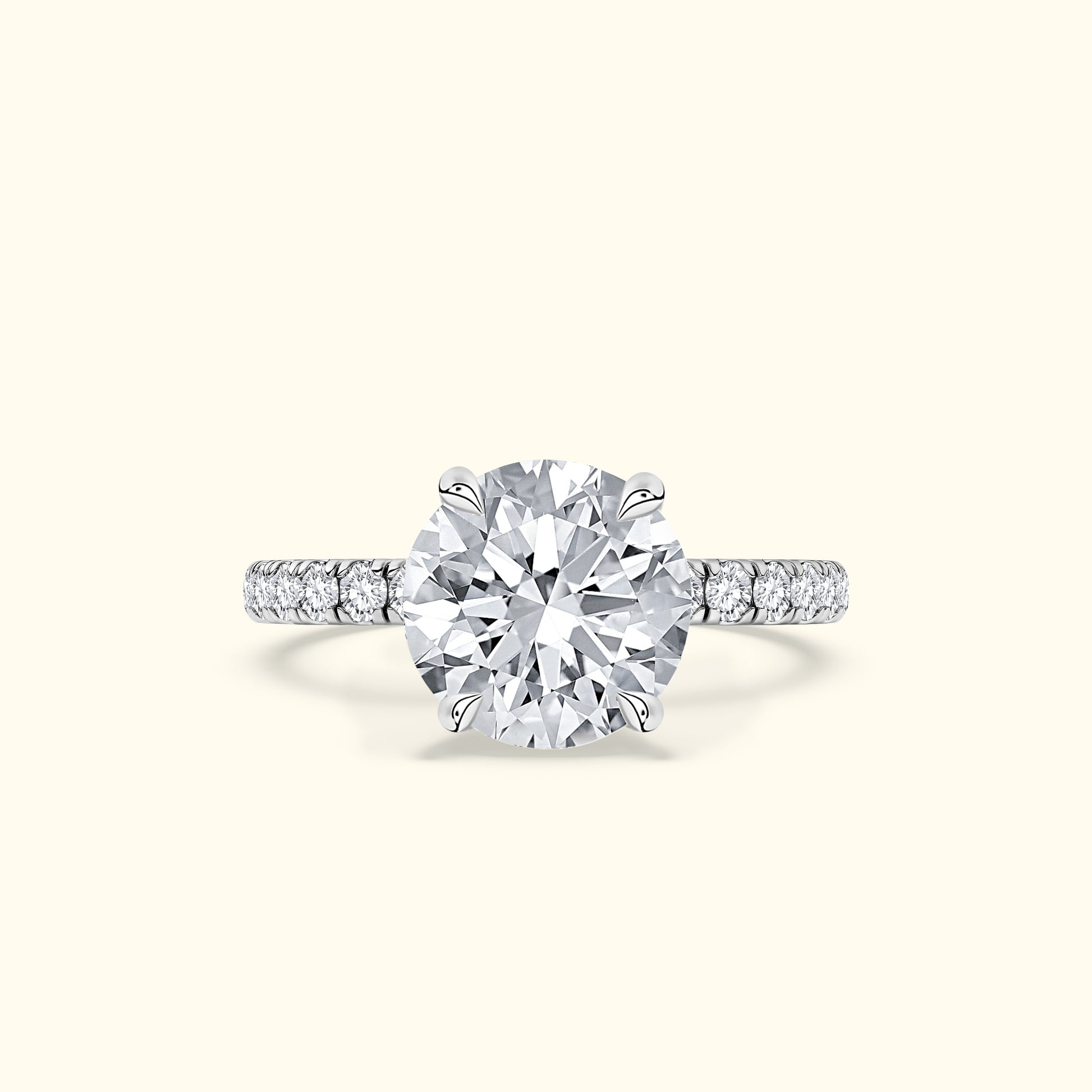 Round diamond engagement ring with a pavé band, set against a soft beige background.