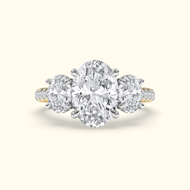 Three-stone engagement ring featuring a large oval diamond center with two round diamonds on each side.