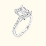 Emerald-cut diamond ring set in white gold with a delicate halo of smaller diamonds.