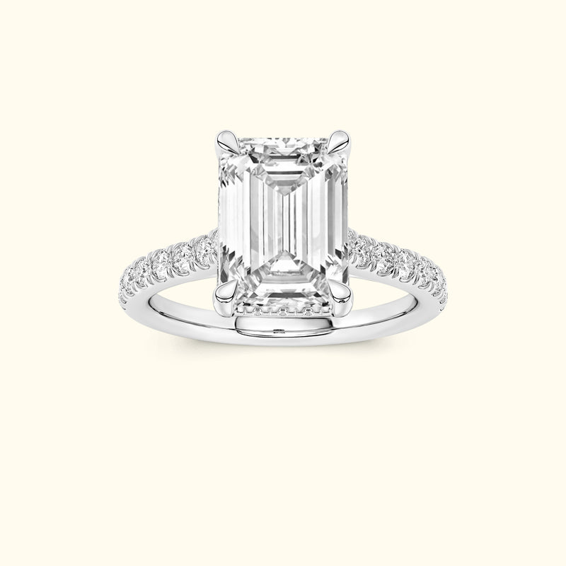Emerald-cut diamond ring with pave-set diamond band on a light background.