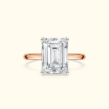 Emerald-cut diamond ring set on a rose gold band against a light background.