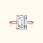 Emerald-cut diamond ring with a rose gold band on a light background.