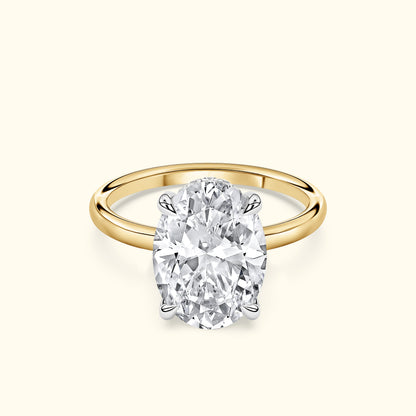 Oval diamond engagement ring with a gold band and silver prongs on a light background.