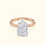 Pear-shaped diamond ring with a rose gold band on a light background.