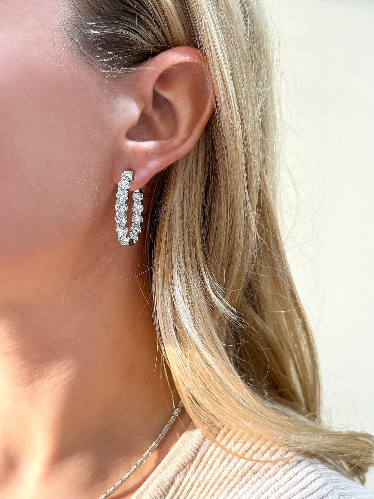 Sparkling diamond hoop earrings worn by a woman with long blonde hair.