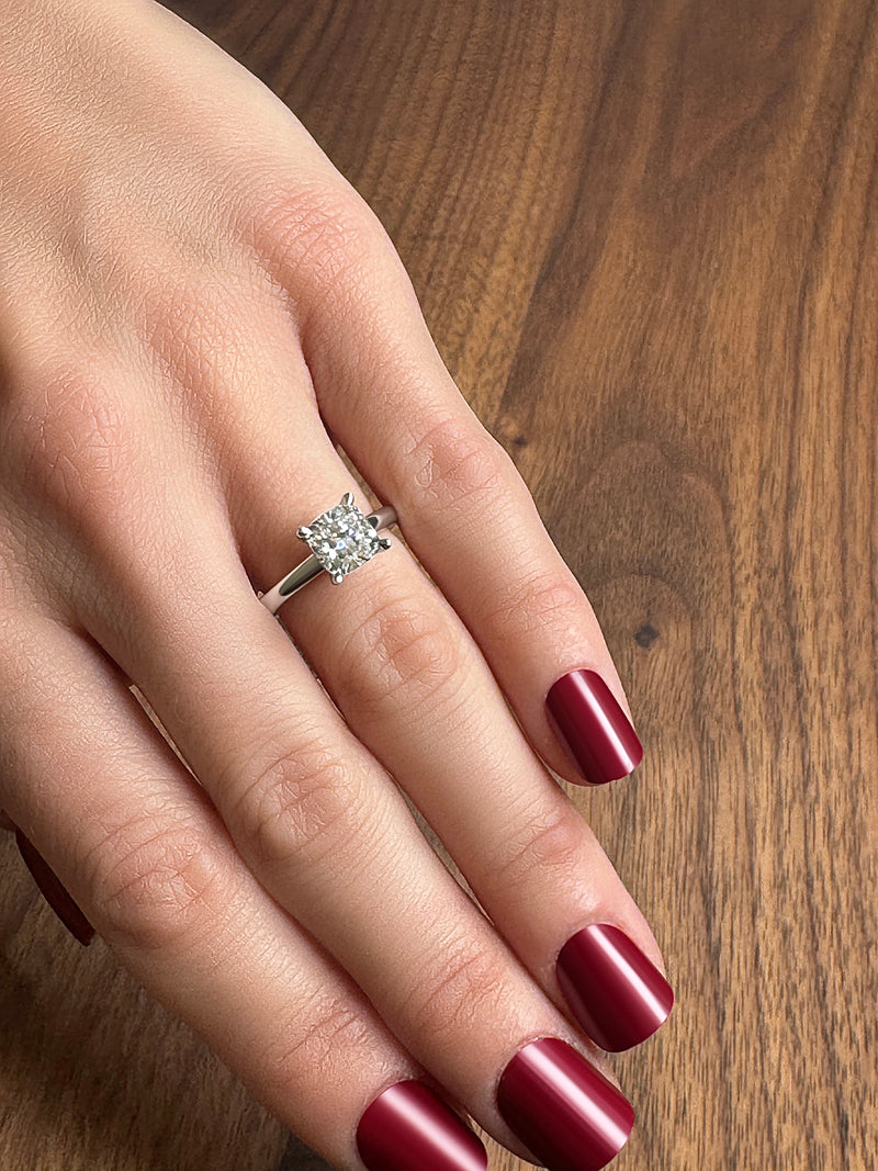 A close-up of a hand displaying a diamond engagement ring on a wooden surface.