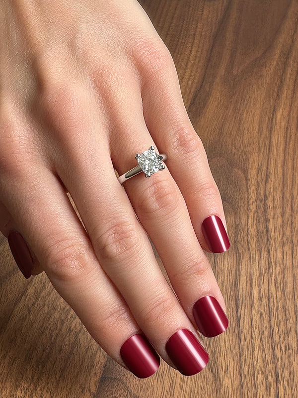 A hand displaying a silver engagement ring with a large square-cut diamond, set against a wooden background.