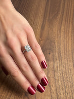 Elegant silver ring with an emerald-cut diamond, worn on a hand with deep red nails.