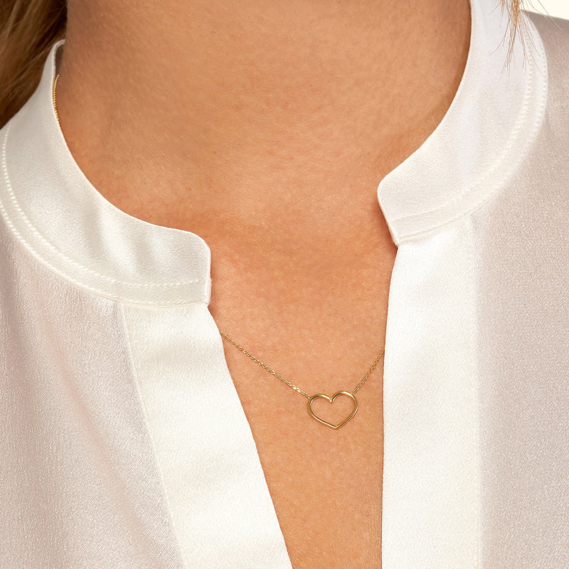 Delicate gold heart pendant resting on a white collared blouse.