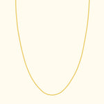 Thin gold necklace elegantly draped against a cream background.
