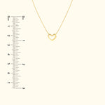 Delicate gold heart pendant necklace on a light background with a ruler for size reference.