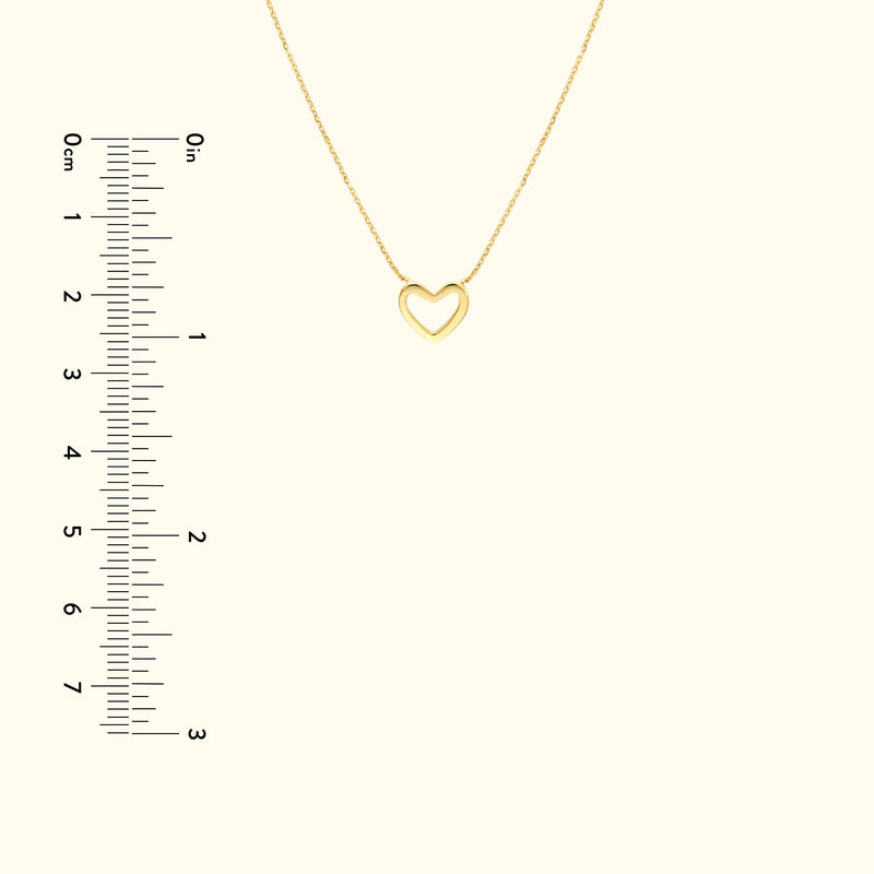 Delicate gold heart pendant necklace on a light background with a ruler for size reference.