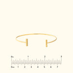 Simple gold cuff bracelet with two vertical ends, set against a light background.