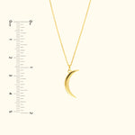Gold crescent moon pendant hanging from a delicate chain, alongside a ruler for scale.