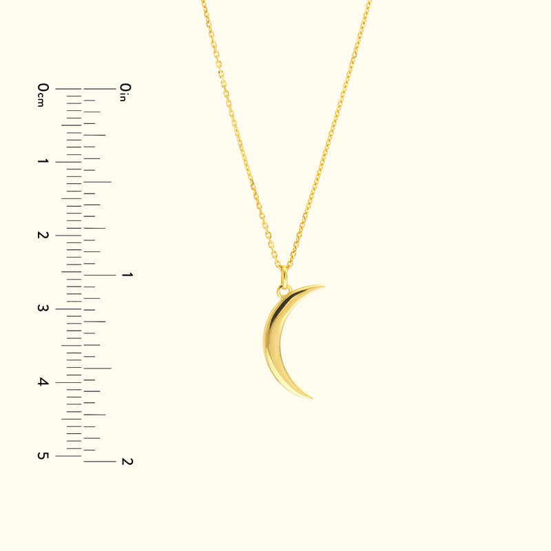 Gold crescent moon pendant hanging from a delicate chain, alongside a ruler for scale.