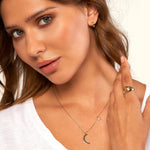 Woman with long hair wearing a crescent moon necklace, star earrings, and a statement ring.
