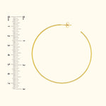 Gold hoop earring next to a ruler for size comparison.