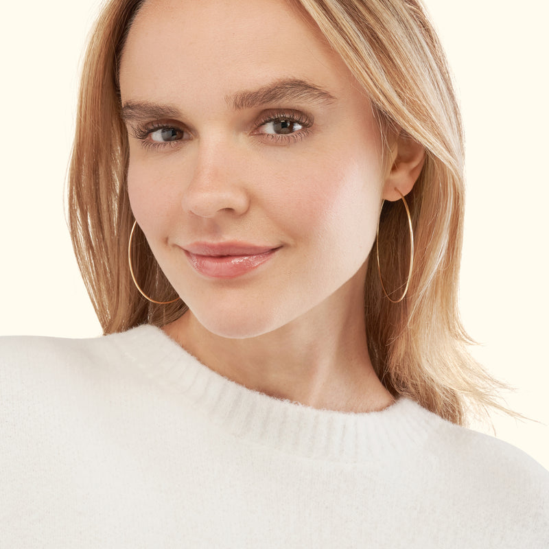 Smiling woman wearing large gold hoop earrings and a white sweater.