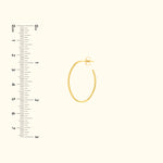 Gold hoop earring with a secure clasp, next to a ruler for size reference.
