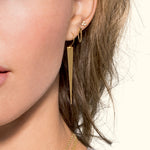 Long gold earrings alongside delicate stud earrings, worn by a woman with soft features.