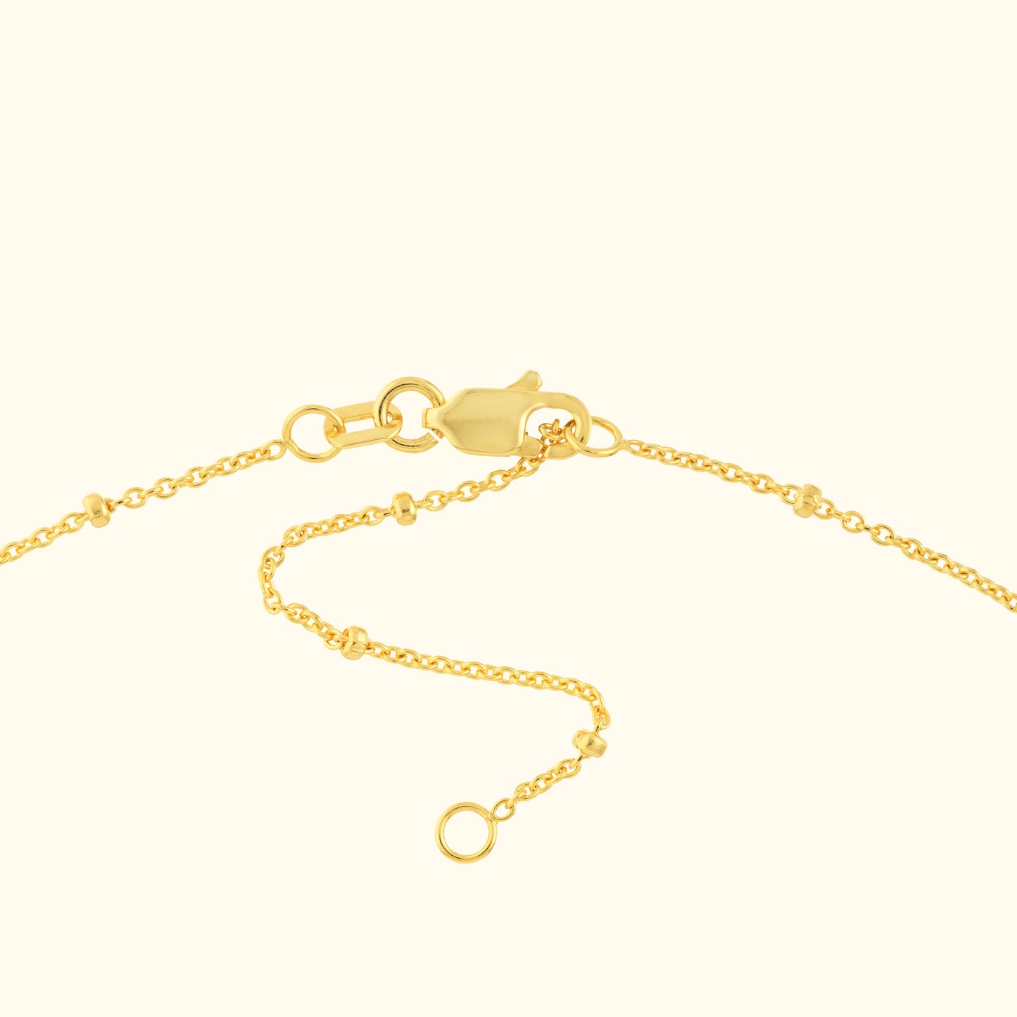 Close-up of a gold necklace chain with a lobster clasp and small embellishments.