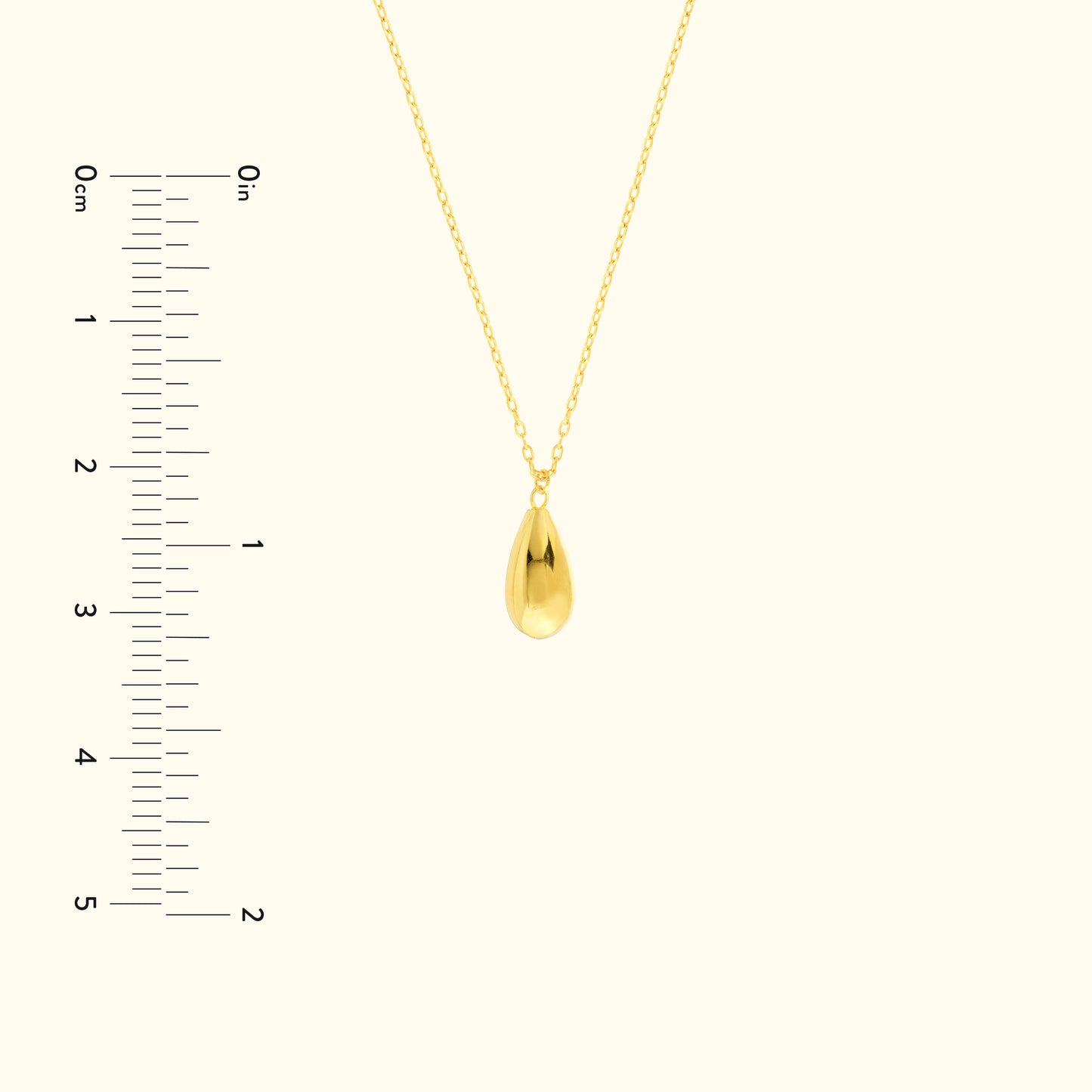 Gold teardrop pendant necklace on a delicate chain, with a measuring scale beside it.