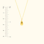 Gold teardrop pendant necklace on a delicate chain, with a measuring scale beside it.