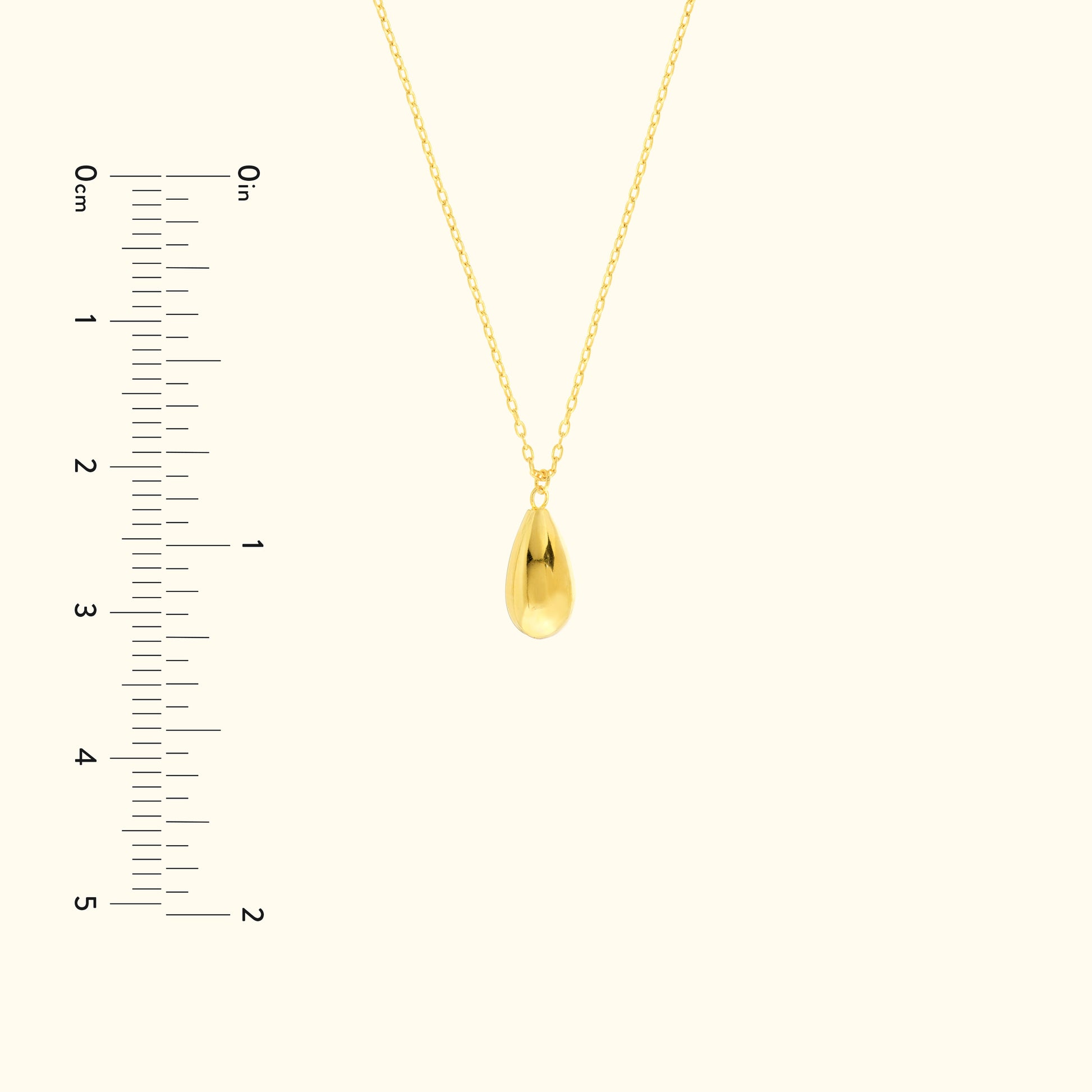 Gold teardrop pendant necklace on a delicate chain, with a measuring scale beside it.