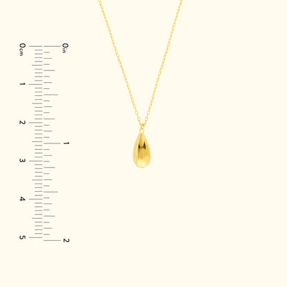 Gold teardrop pendant necklace on a delicate chain, with a measuring scale beside it.