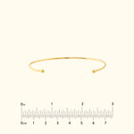 Simple gold cuff bracelet with rounded ends, set against a neutral background.
