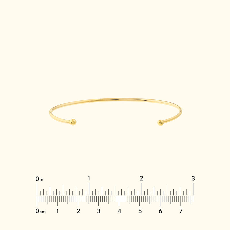 Simple gold cuff bracelet with rounded ends, set against a neutral background.
