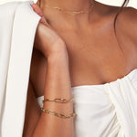 Gold chain bracelet and layered necklaces accessorize a model in a white outfit.