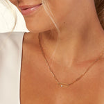 Gold chain necklace with rectangular links and a small white accent, worn by a woman.