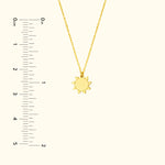 Gold sun pendant necklace on a delicate chain, with a ruler for size reference.