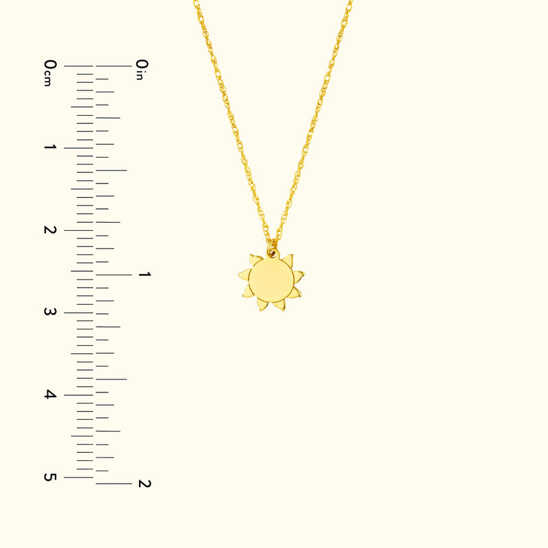 Gold sun pendant necklace on a delicate chain, with a ruler for size reference.