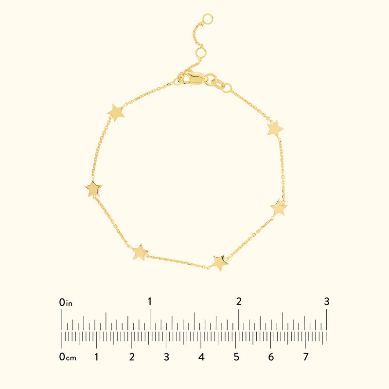 Gold star bracelet on a light background, with a ruler for size reference.