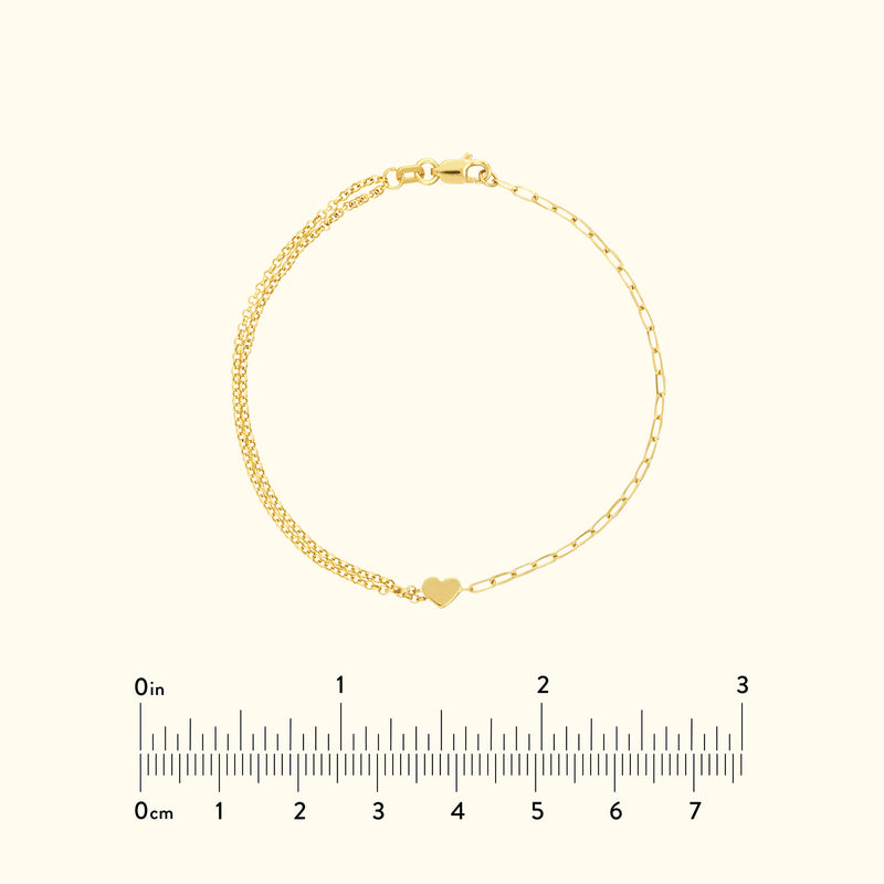 Delicate gold bracelet with a small heart charm, laid against a light background.