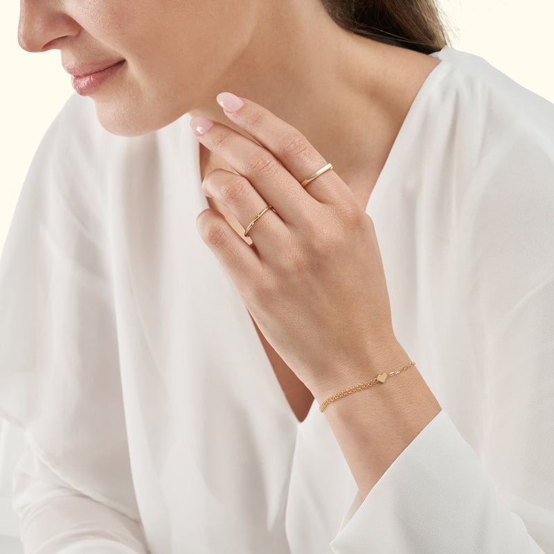 A woman in a white blouse showcases delicate gold rings and a bracelet.