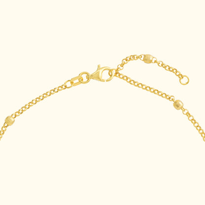 Close-up of a yellow gold necklace chain with a lobster clasp and small beads.