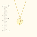 Gold pendant necklace featuring a crescent moon and stars, with a measuring ruler beside it.