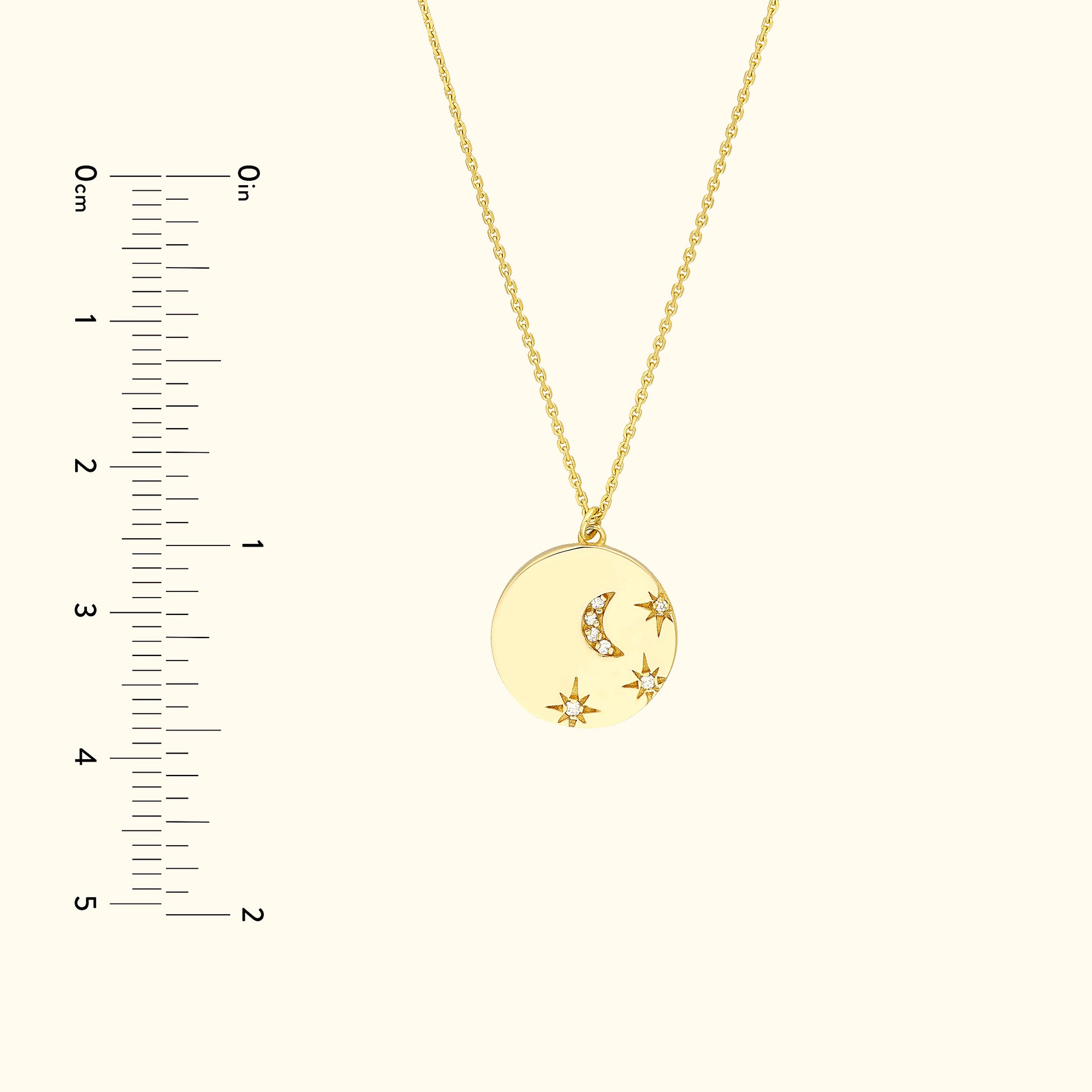 Gold pendant necklace featuring a crescent moon and stars, with a measuring ruler beside it.