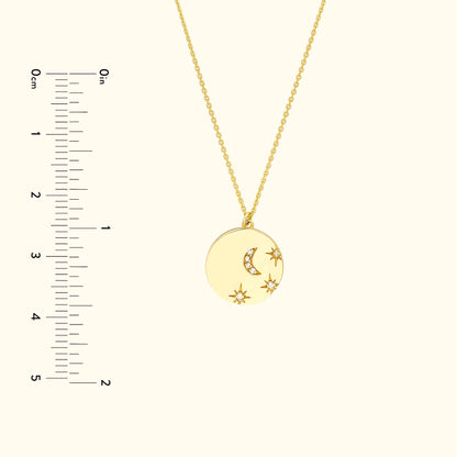 Gold pendant necklace featuring a crescent moon and stars, with a measuring ruler beside it.