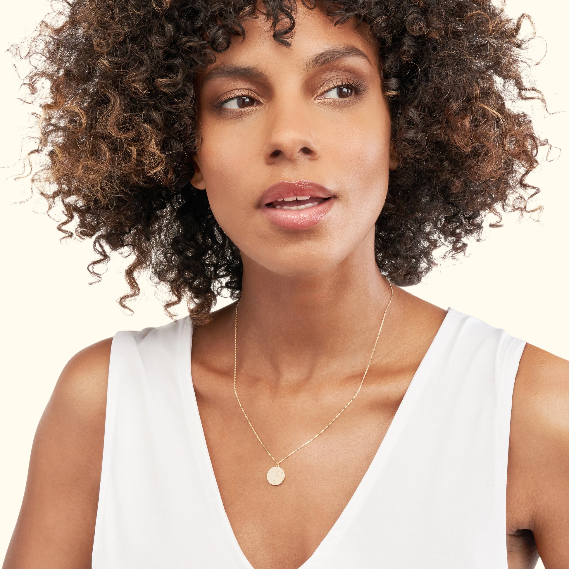 Model wearing a delicate gold necklace with a circular pendant, against a light background.