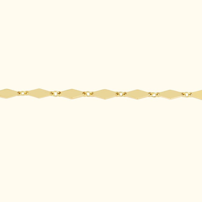 Gold chain bracelet with diamond-shaped links against a soft beige background.