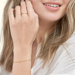 A close-up of a woman’s hand wearing a delicate gold bracelet and a simple ring.