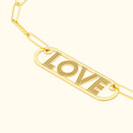 Gold bracelet featuring a rectangular charm with the word "LOVE" engraved.