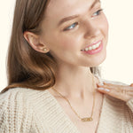 Smiling woman wearing a gold "LOVE" necklace and matching earrings, cozy sweater.
