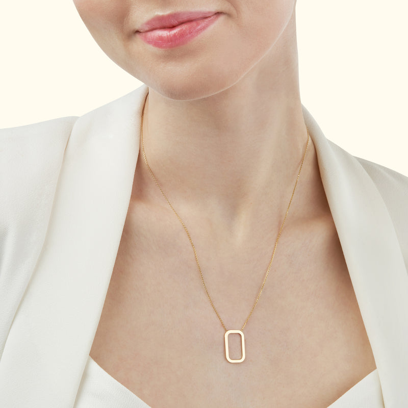Gold necklace with a rectangular pendant, worn by a woman in a white outfit.