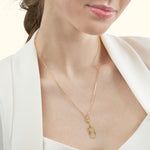 Gold chain necklace with a unique double pendant, worn by a woman in a white blazer.